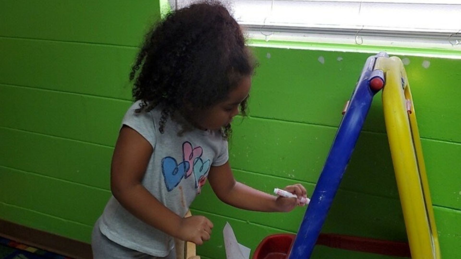 Child playing with a colorful playground structure indoors against a bright green wall.