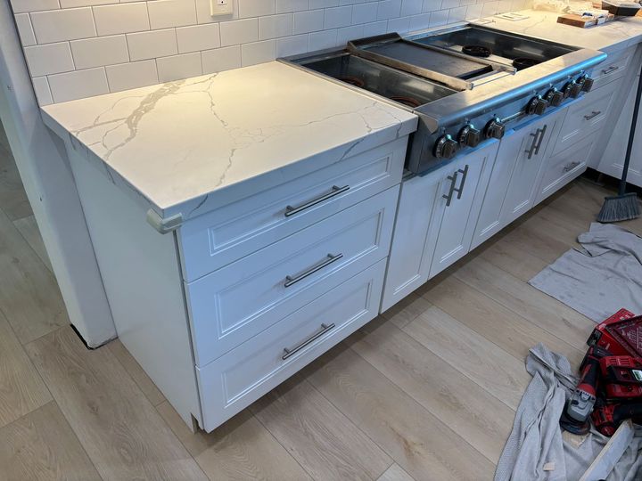 White kitchen counter with a stainless-steel stove and drawers, showing a crackled countertop surface.