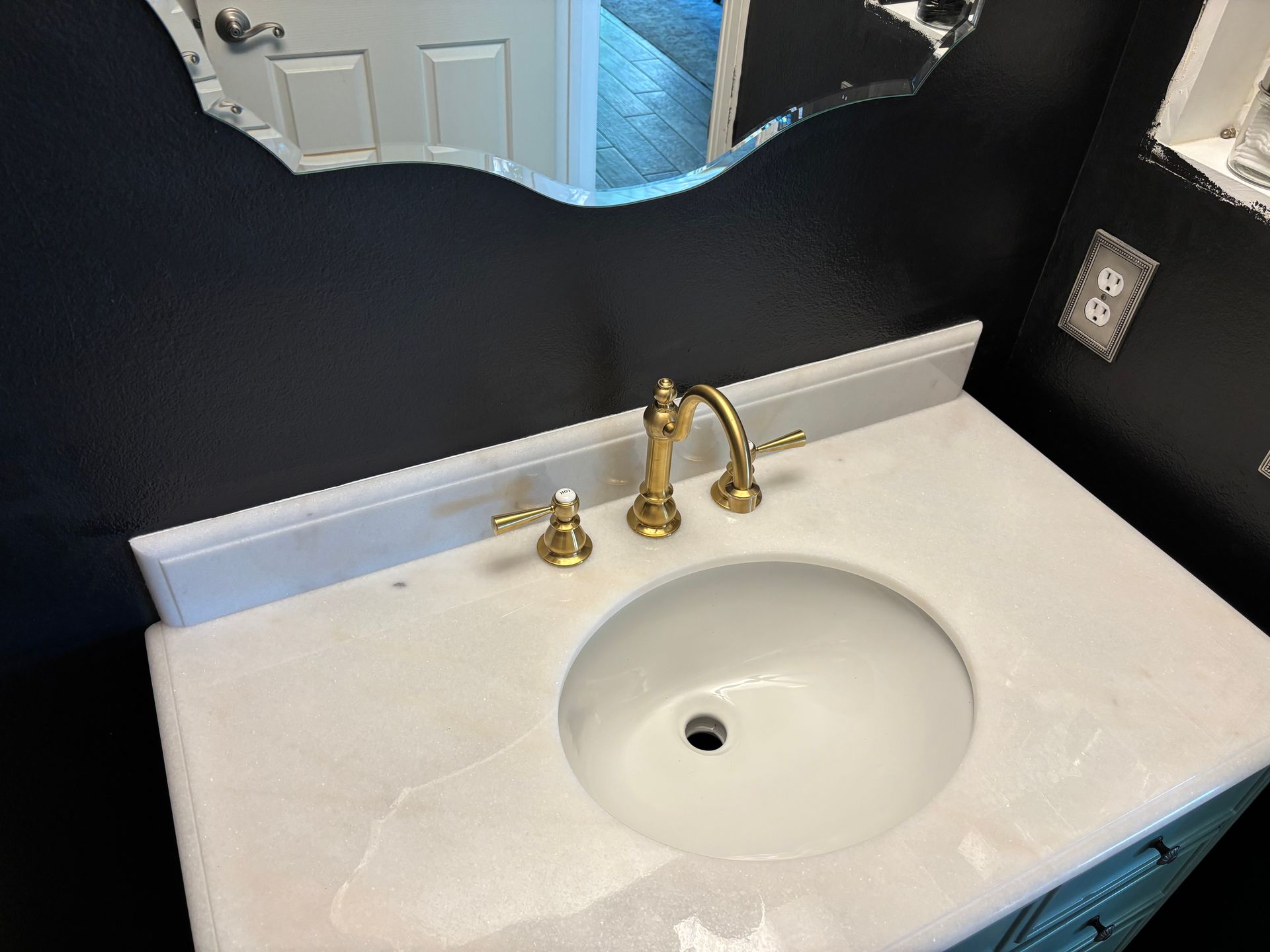 White bathroom vanity with round sink, gold faucet, and black-and-white mirror backsplash