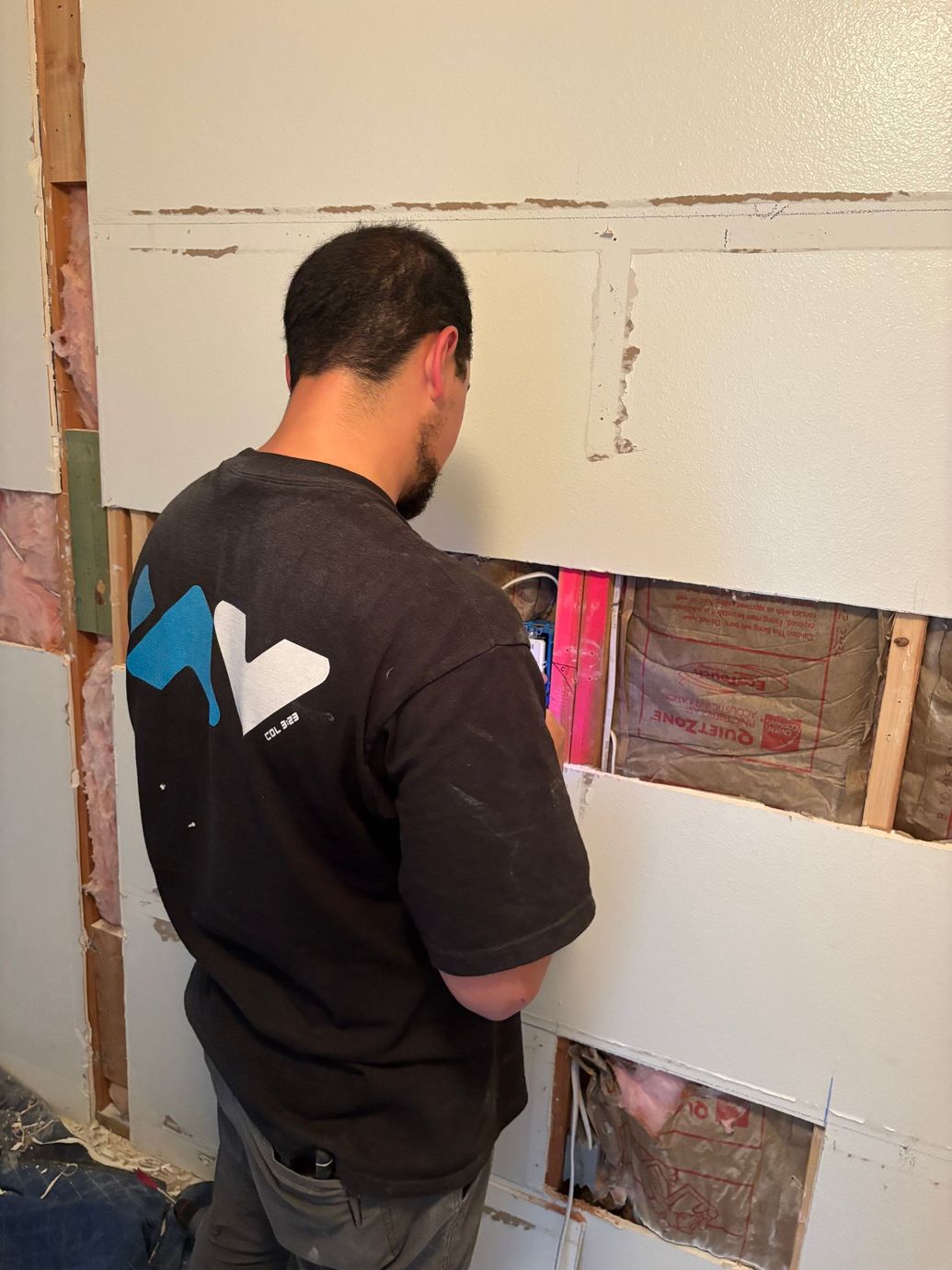 Person installing white wall panels in a partially exposed room with visible studs.