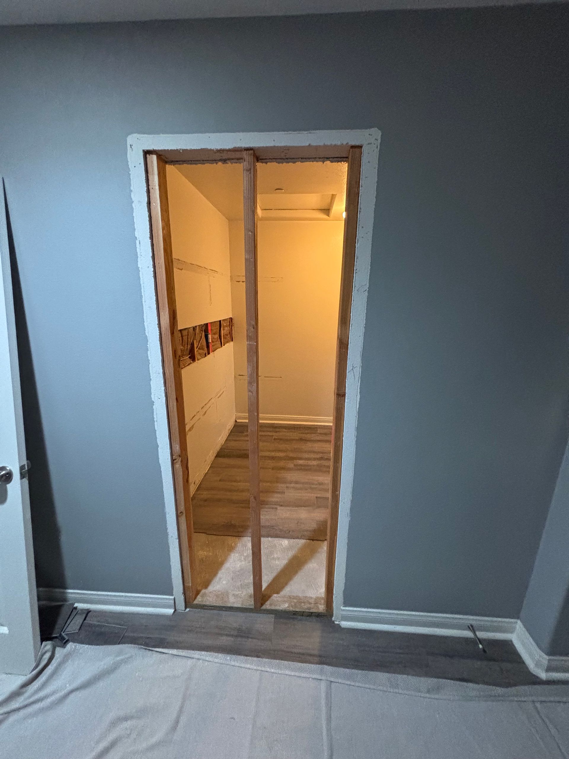 Interior doorway with exposed framing and warm light, viewed from a gray room with protective floor covering