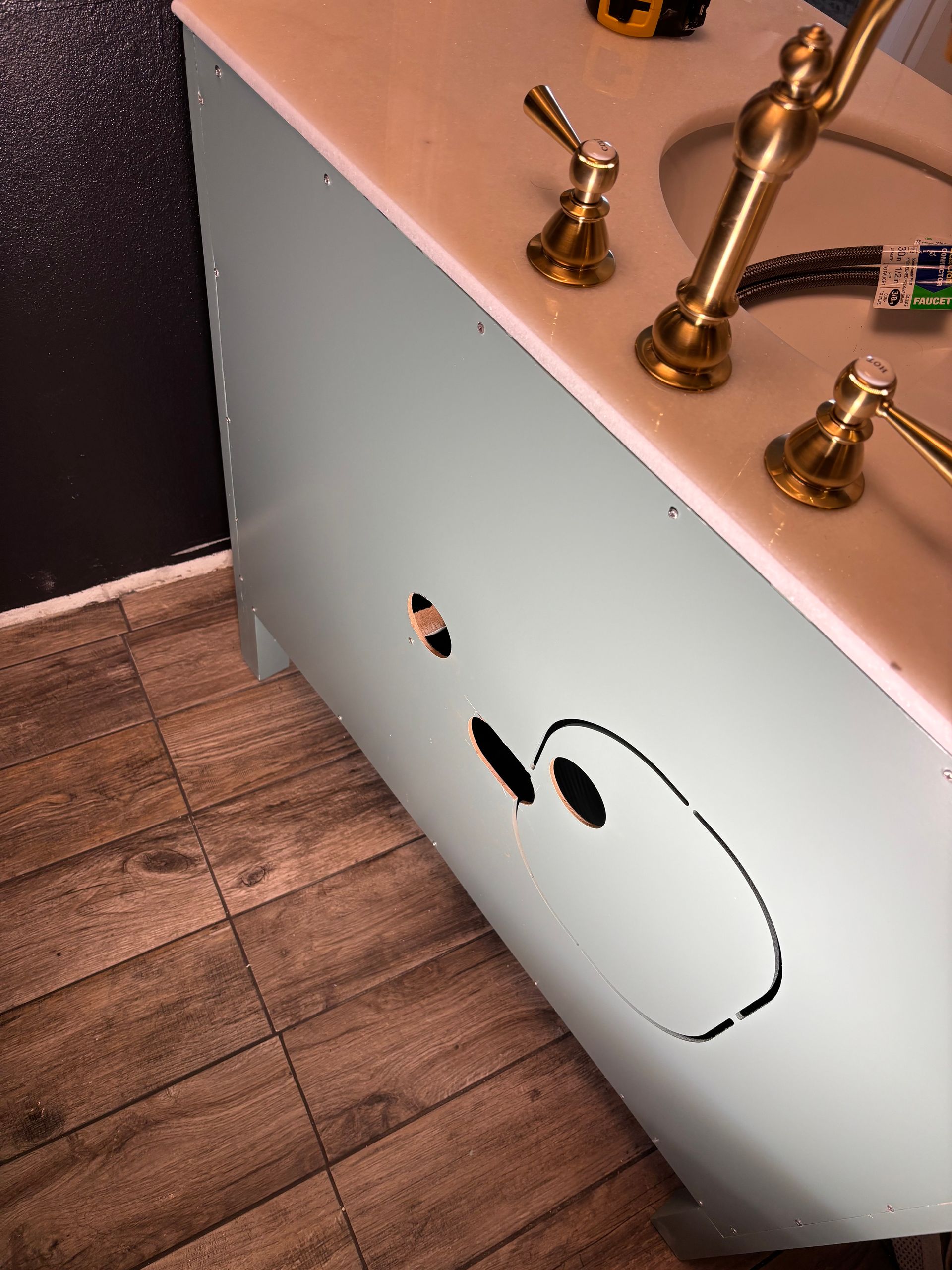 Under-sink cabinet with a black smiley face drawn on the white panel beside a bathroom vanity.