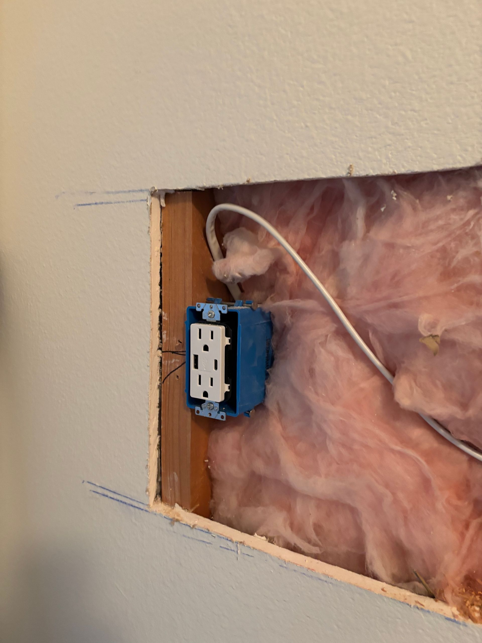 Blue electrical box in wall cavity with insulation and white wires exposed