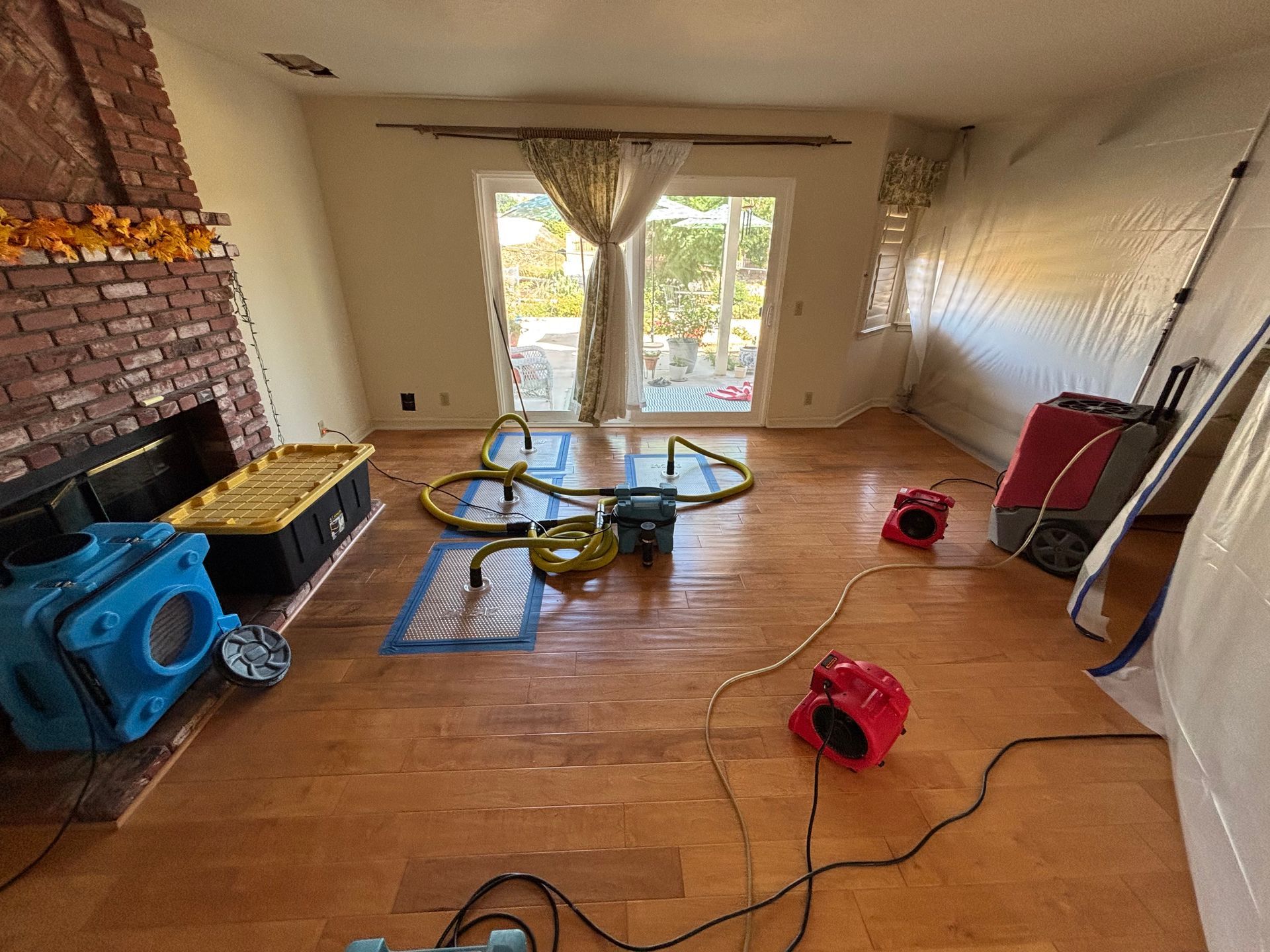 Living room with wood floors, scattered cleaning tools, and open doors to a sunny patio