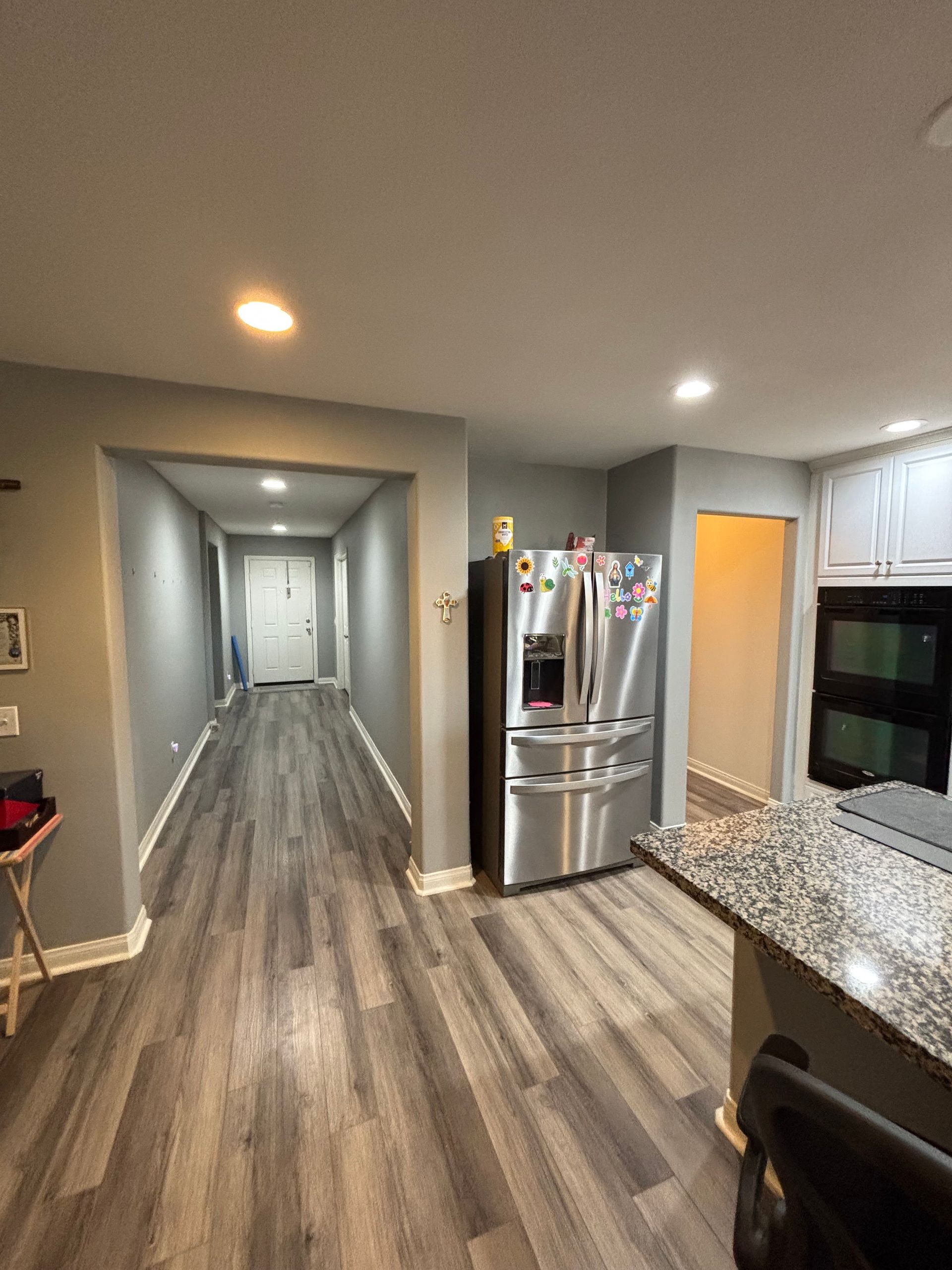 Modern kitchen and hallway with gray wood floors, stainless fridge, granite counter, and recessed lights