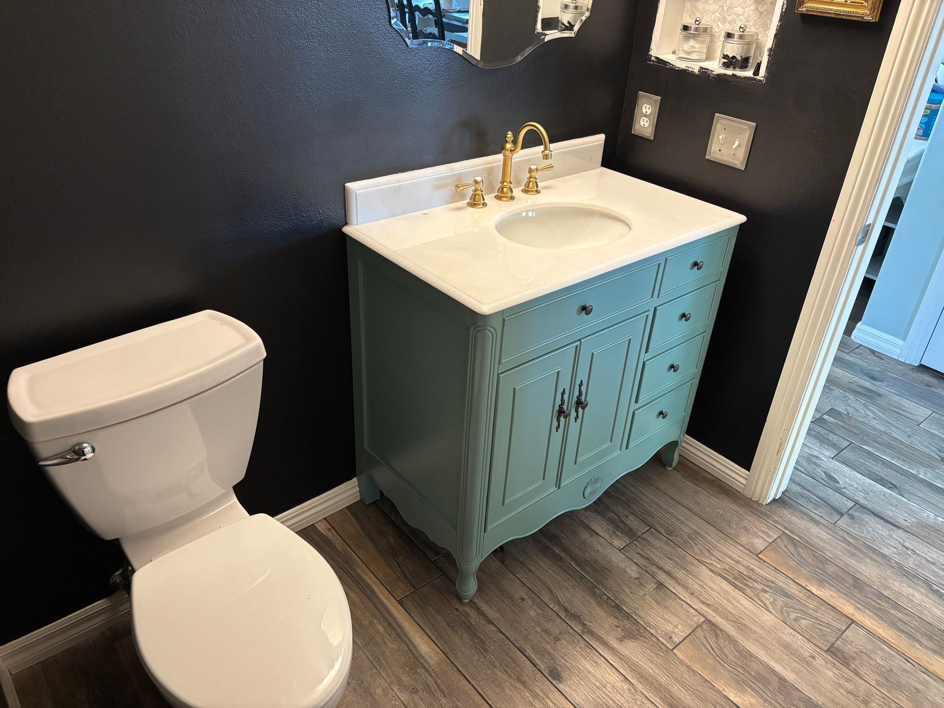 Bathroom with white toilet and teal vanity with white sink on wood-look floor