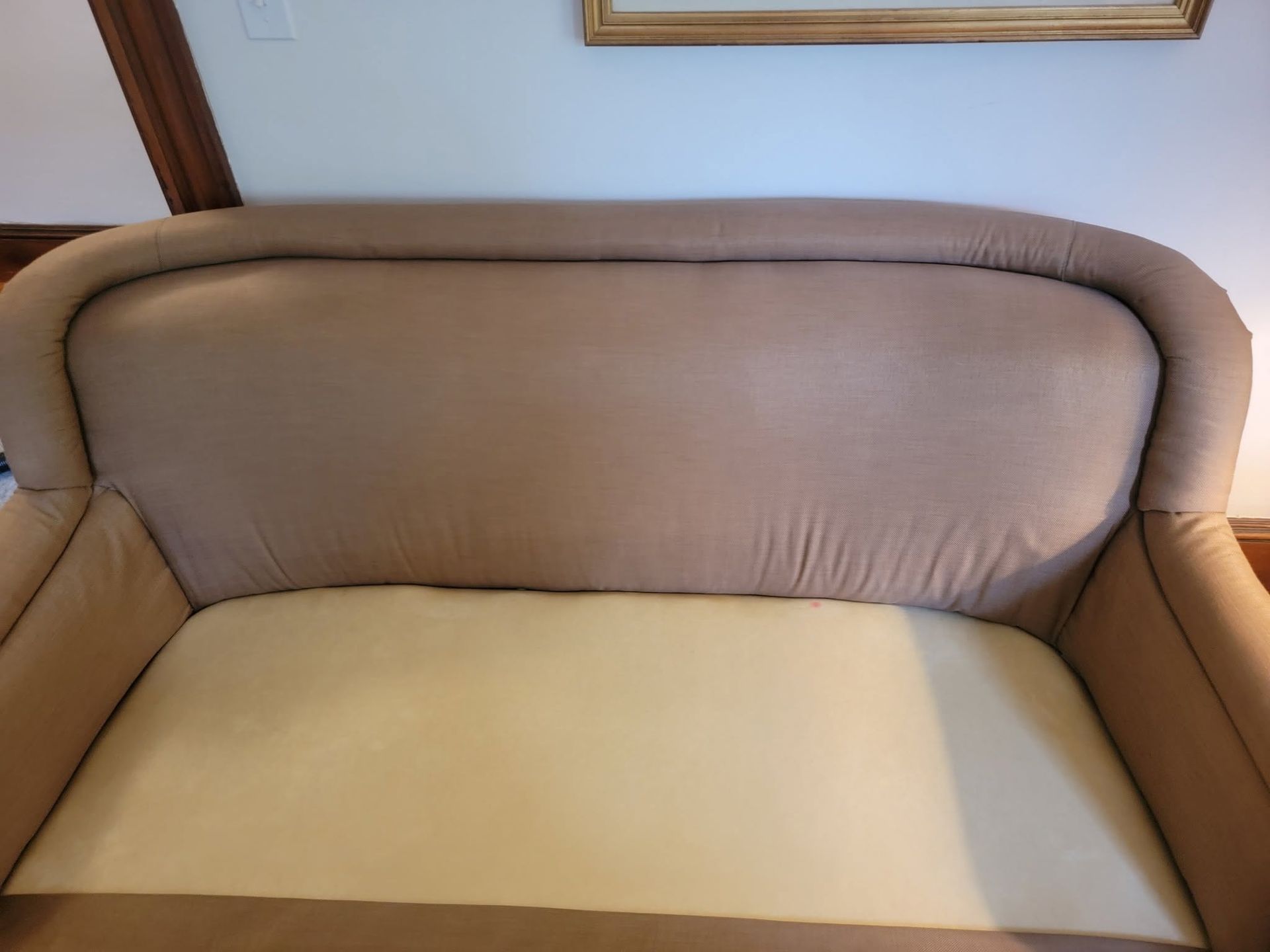 Beige upholstered couch with a light-colored seat cushion against a wall.