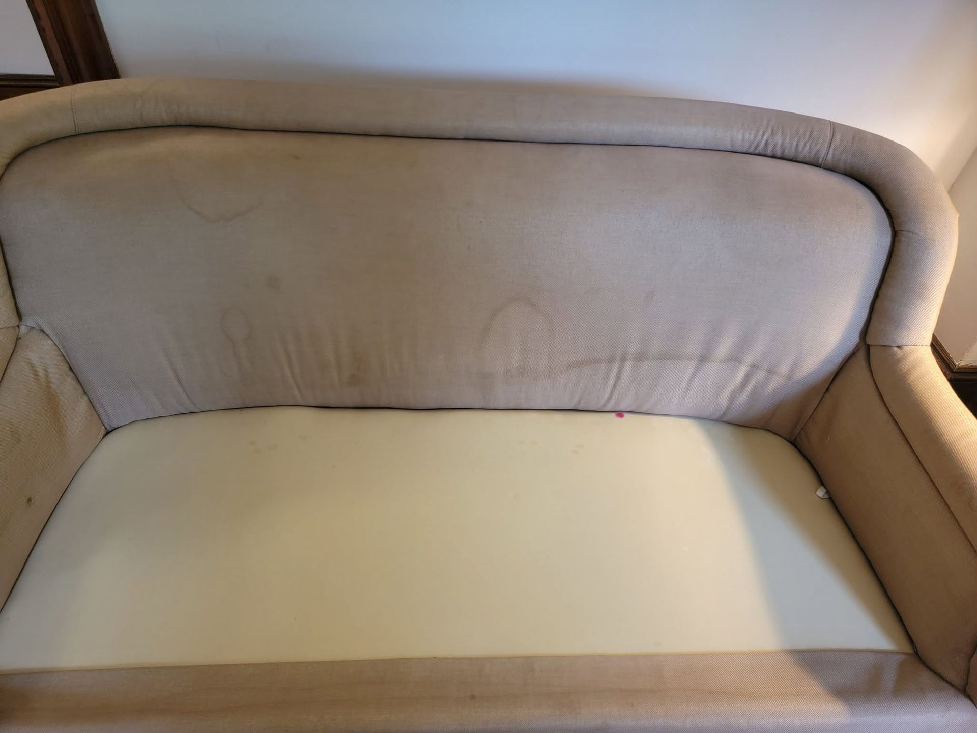 Beige upholstered armchair with worn seat cushion and curved backrest