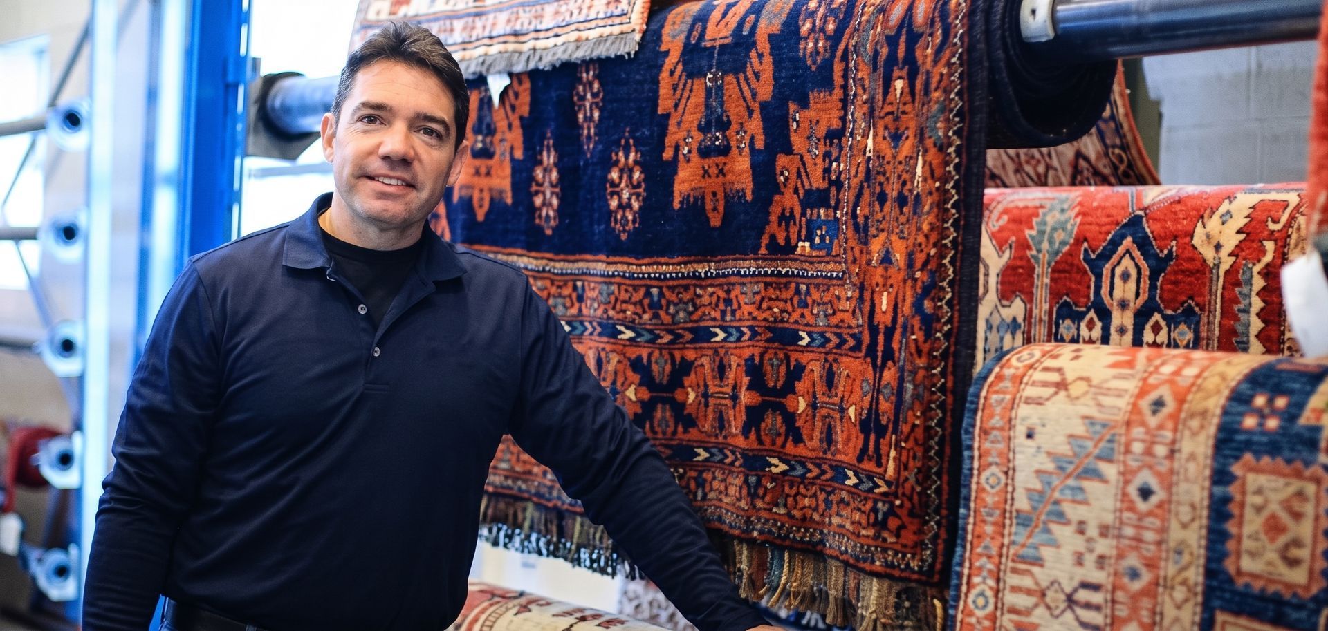Man standing beside colorful patterned rugs in a shop, smiling at the camera.