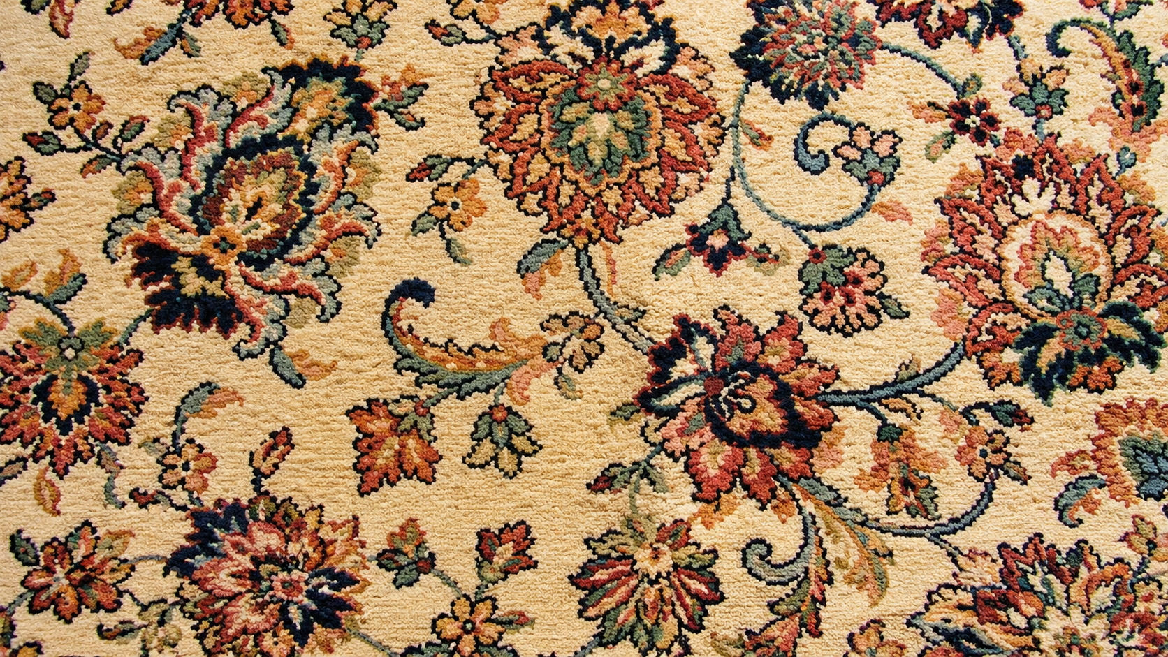 Close-up of a floral patterned rug in beige, pink, green, and dark blue tones