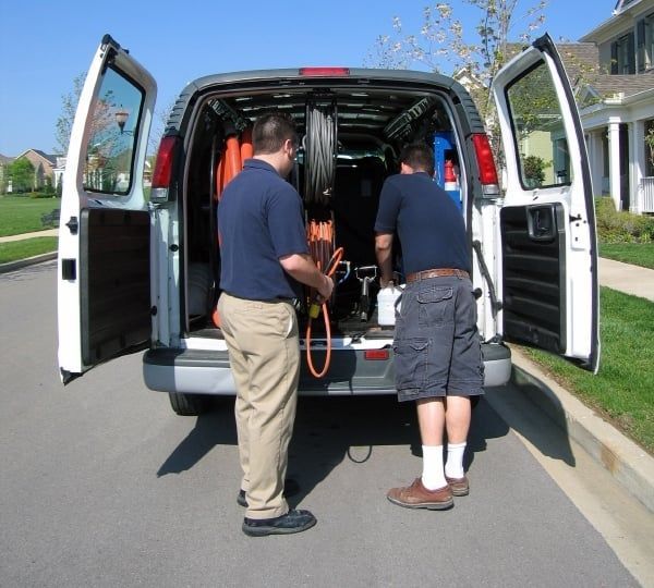 Two men loading equipment into the back of a white van on a residential street