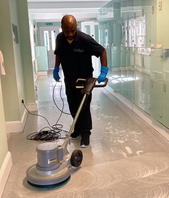 Worker polishing a hospital hallway floor with a floor buffer and blue gloves
