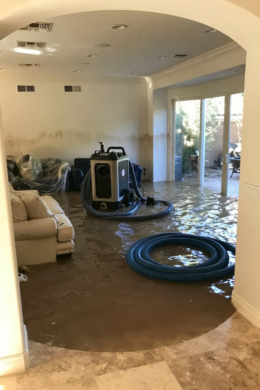 Flooded living room with standing water, carpet, and a water extraction machine near a sliding glass door