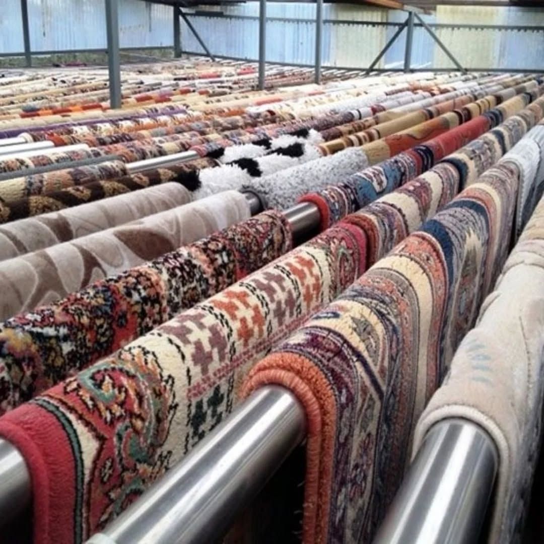 Rows of patterned rugs drying on metal racks in a warehouse-like space