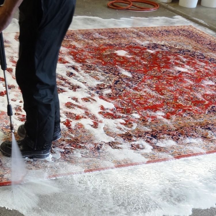 Person pressure-washing a red patterned rug indoors with white foam