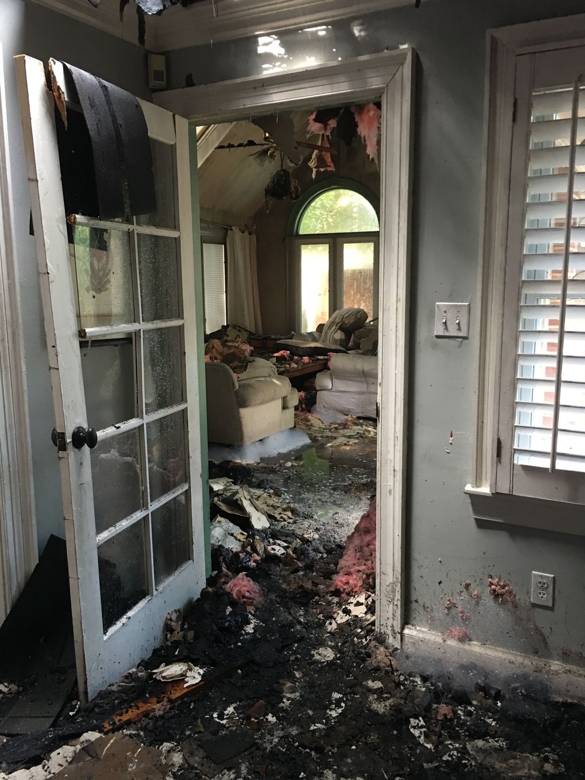 Burned hallway doorway with heavy fire damage and debris inside a damaged home
