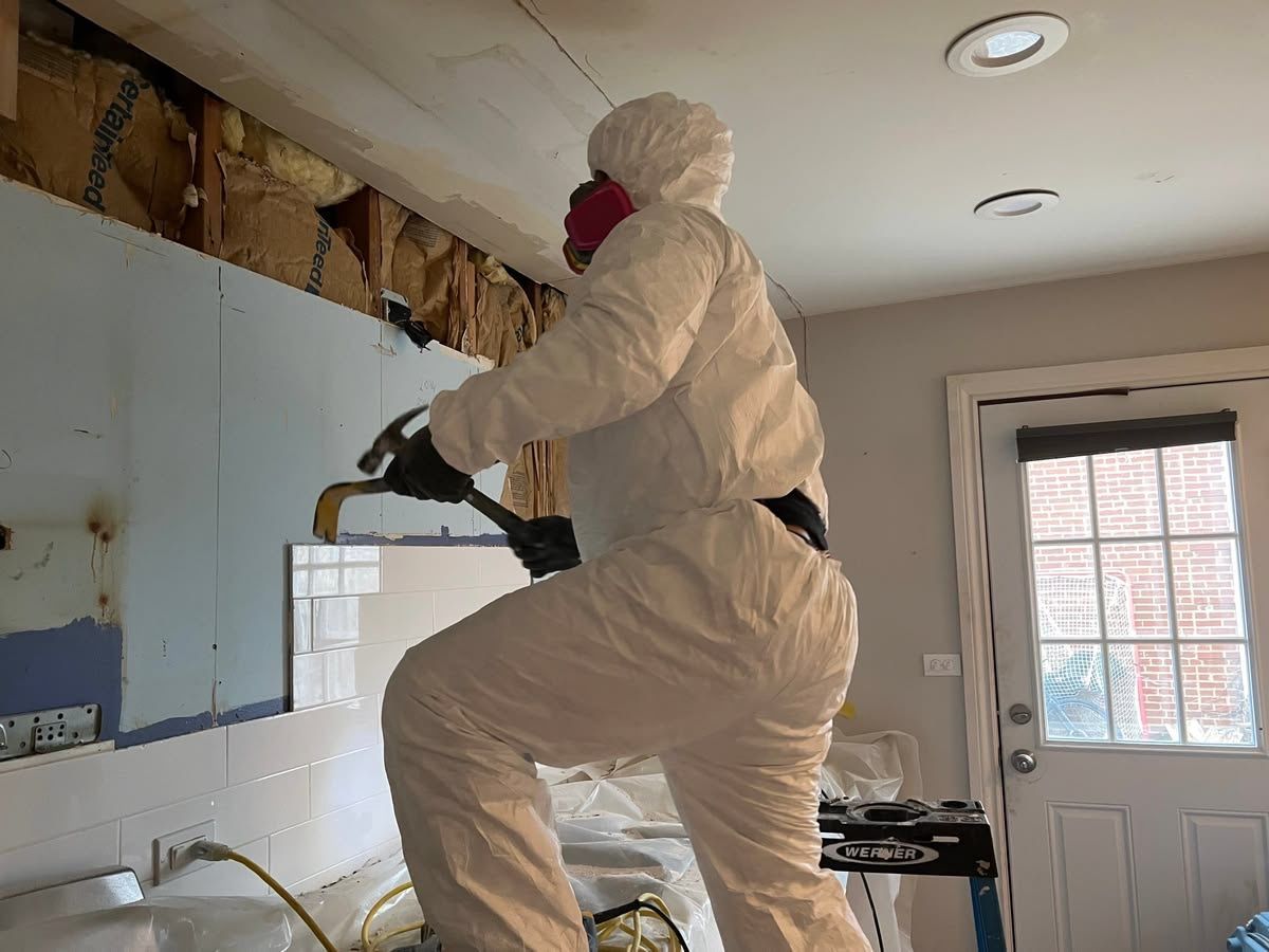 Person in white protective coveralls spraying a wall during indoor renovation.