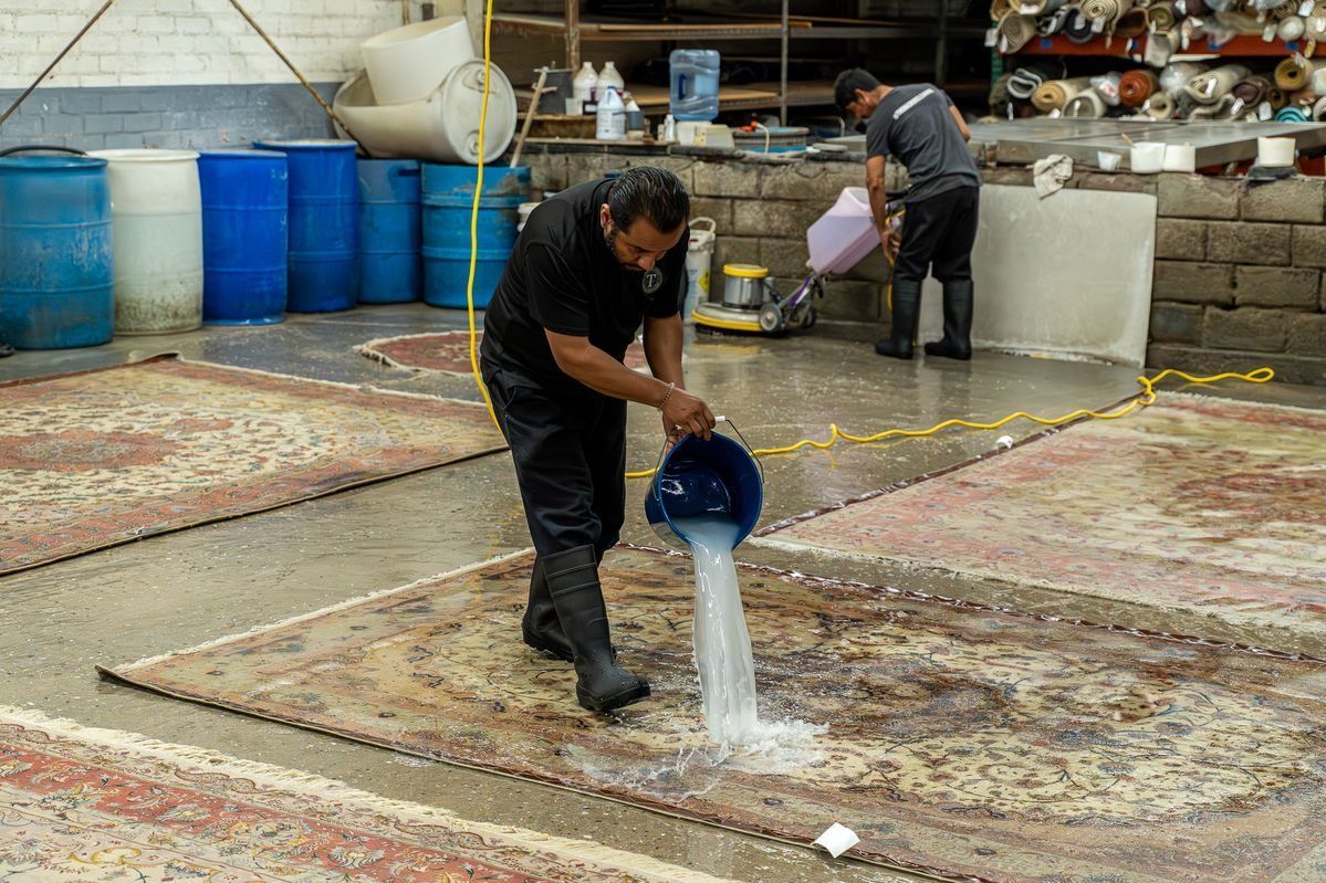 Worker pouring water from a blue bucket onto a wet floor in an industrial area
