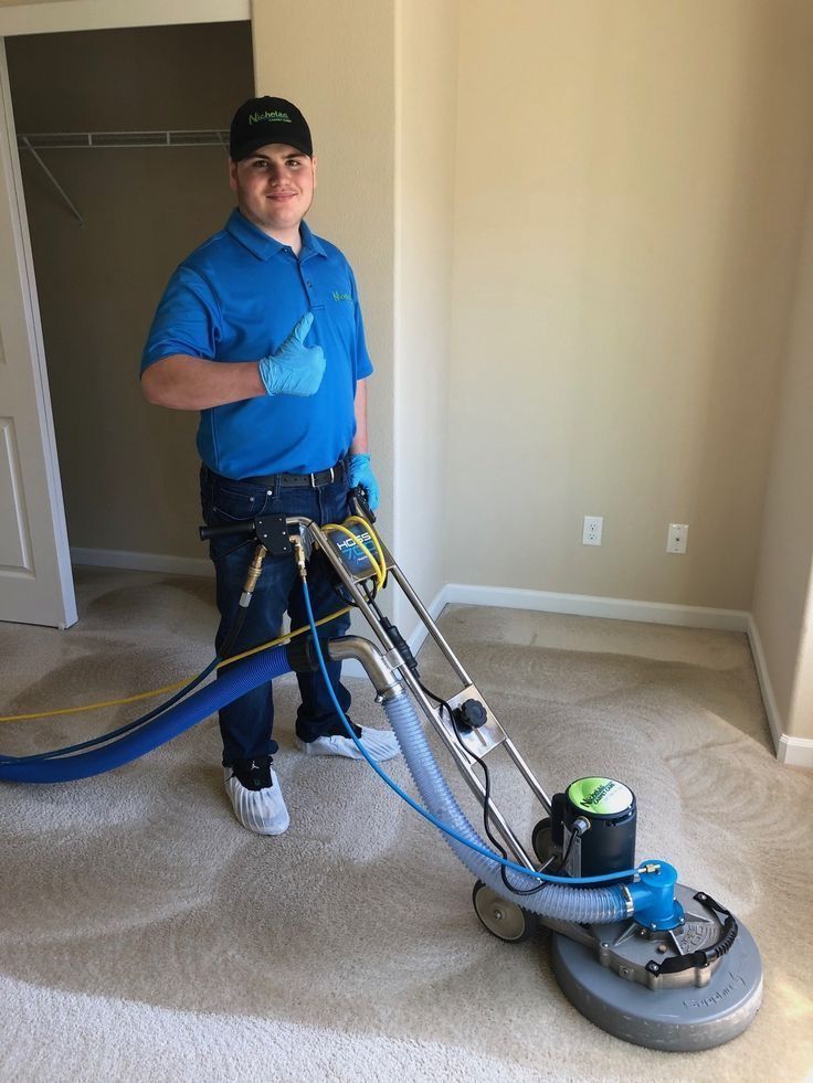 Worker using a floor buffer to clean beige carpet in an empty room