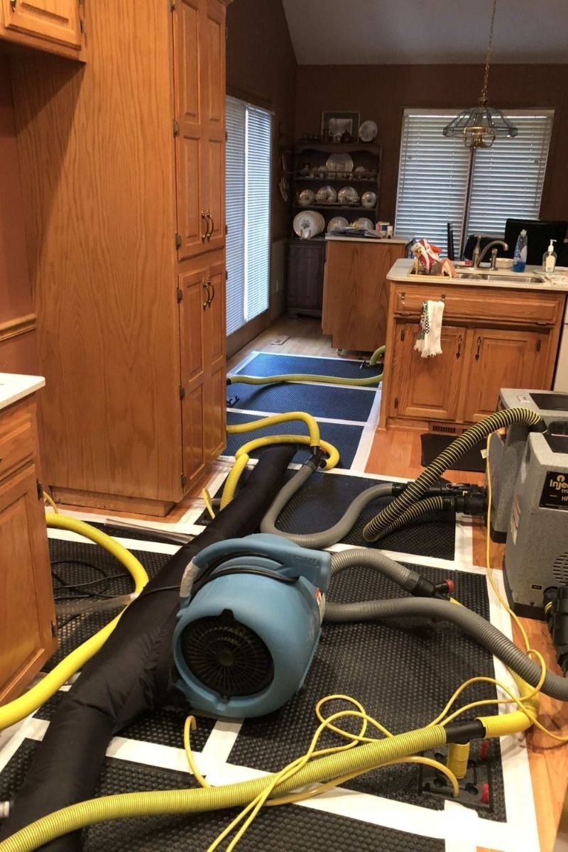 Kitchen with water-damage cleanup gear, including an air mover, dehumidifier, and hoses on the floor.