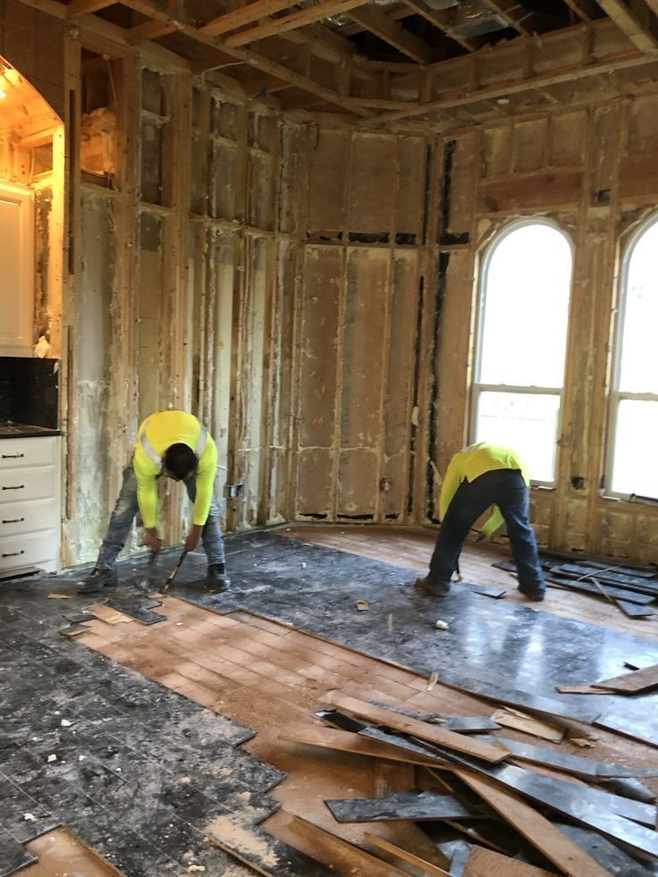 Two workers in high-visibility vests tearing up flooring inside a stripped-down room.