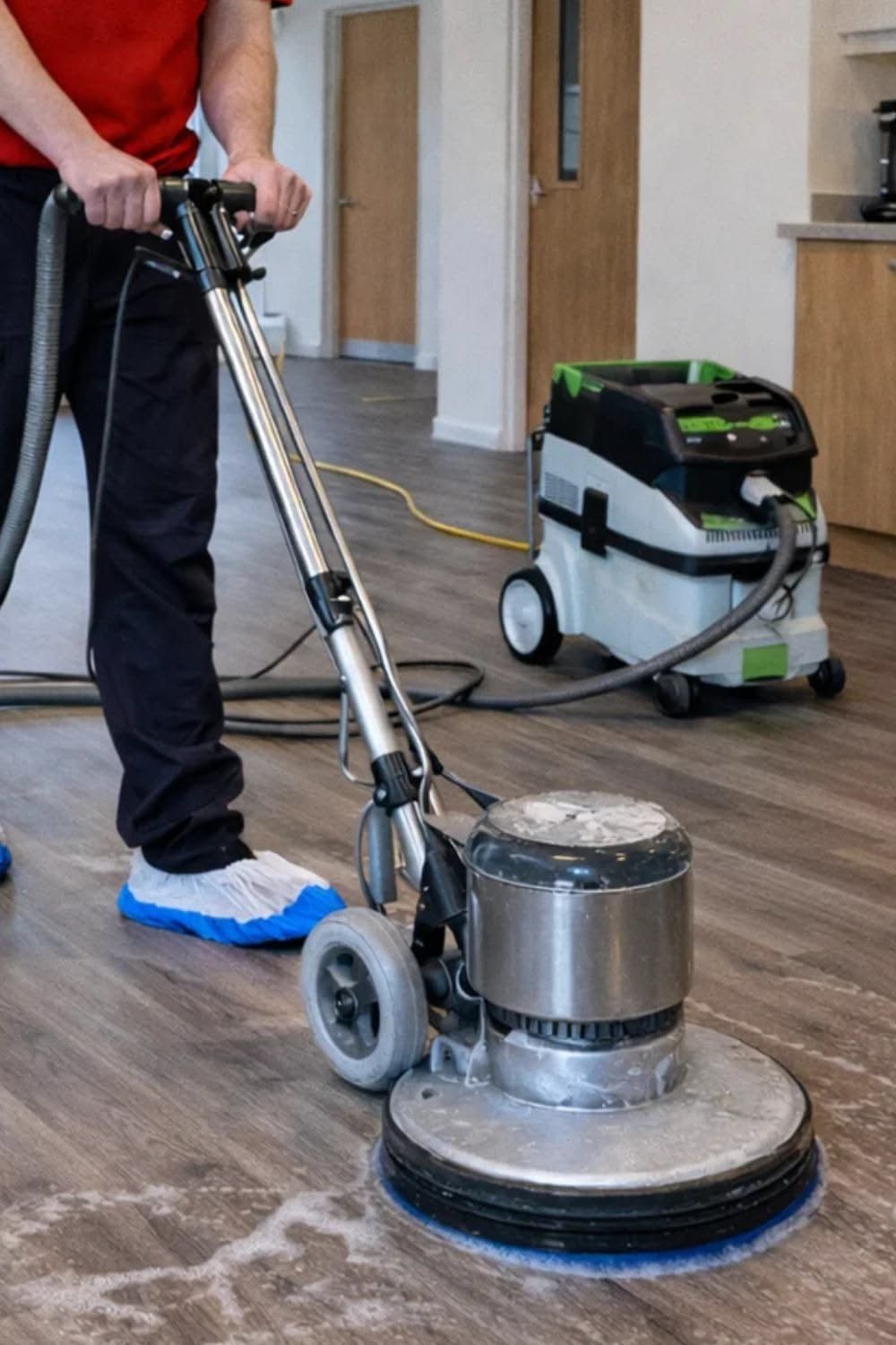 Worker using a floor buffer on a wooden floor beside a cleaning machine