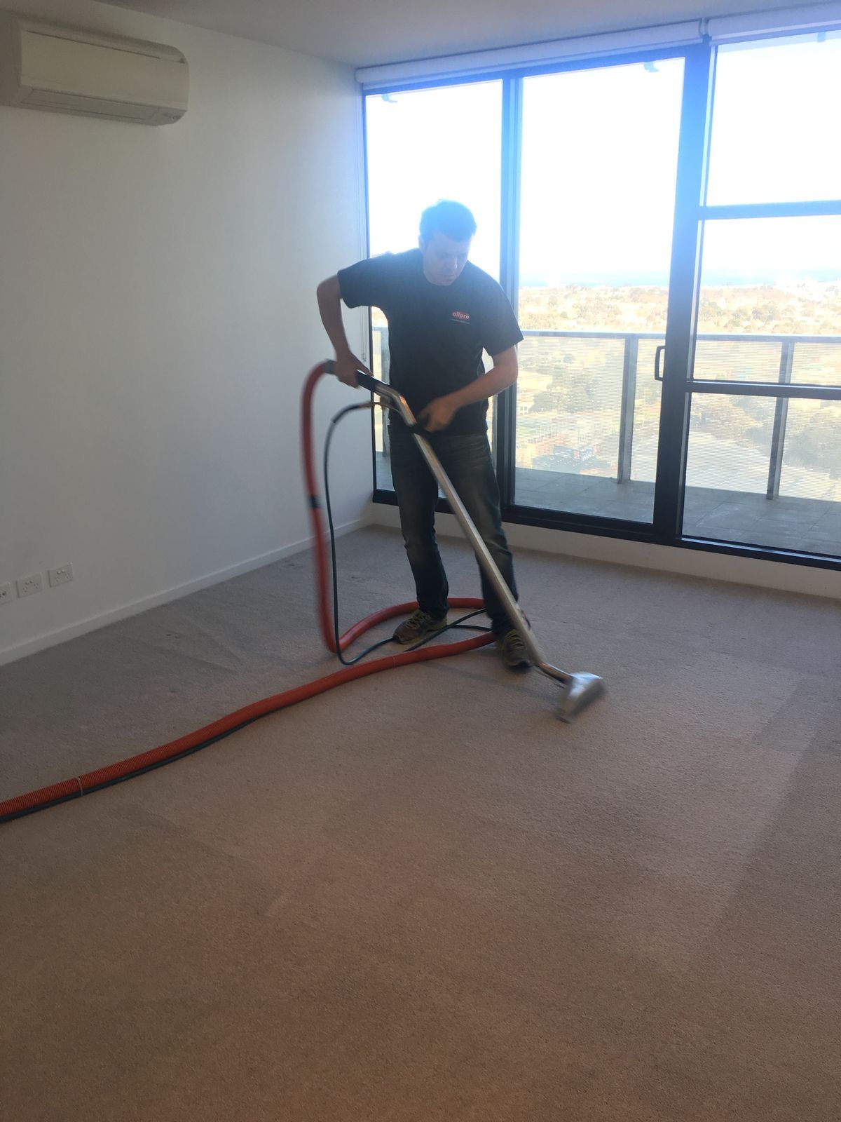 Person vacuuming carpet in a bright room with large windows