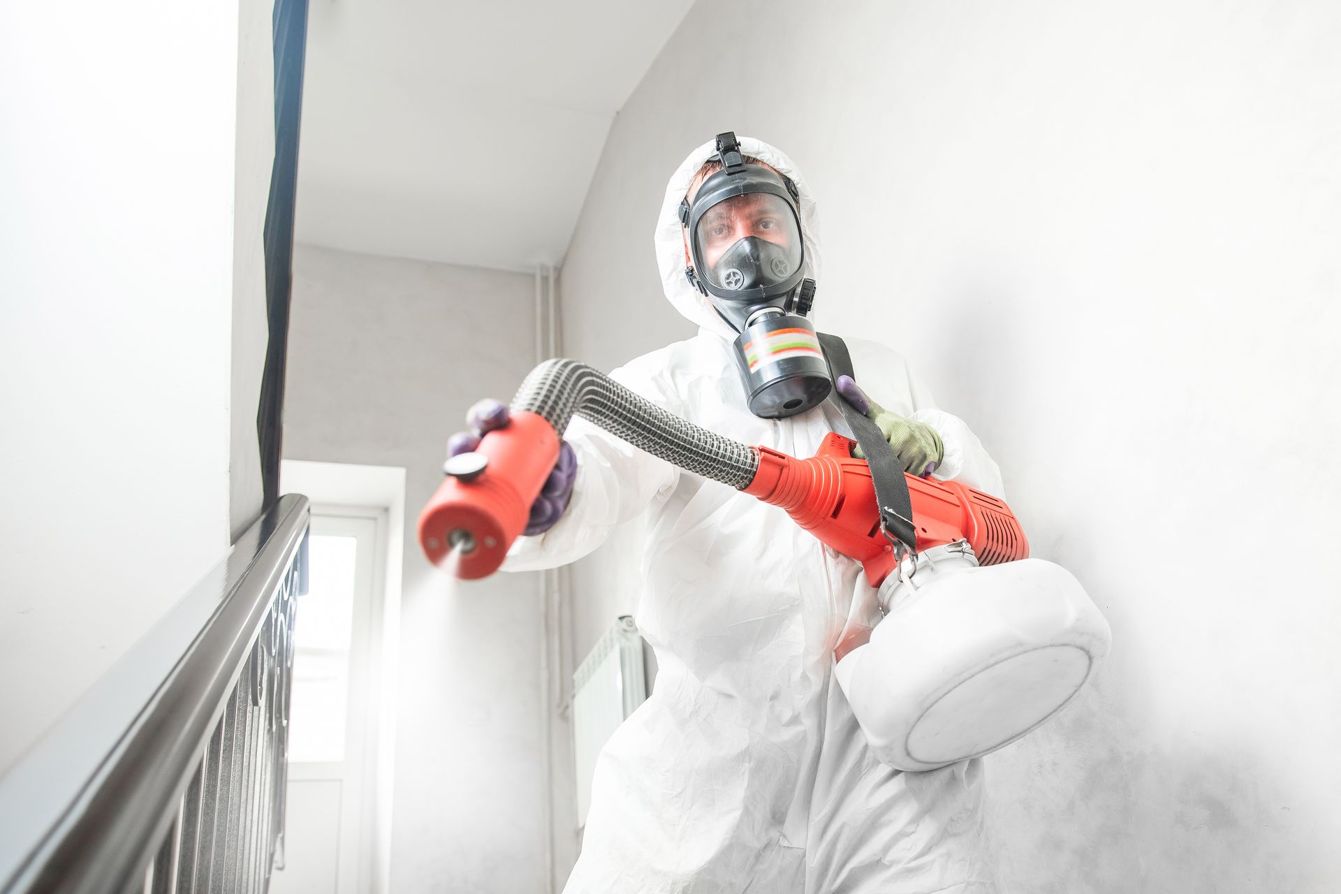 Person in hazmat suit, respirator, spraying disinfectant in a building.