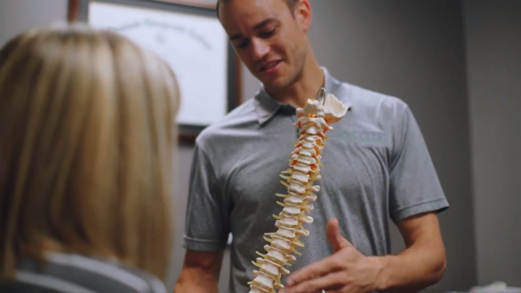 Doctor explaining a spine model to a seated patient in a clinic