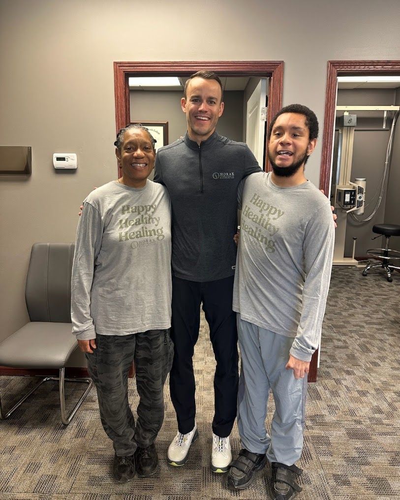 Three people posing indoors in front of mirrors, wearing matching gray long-sleeve shirts.