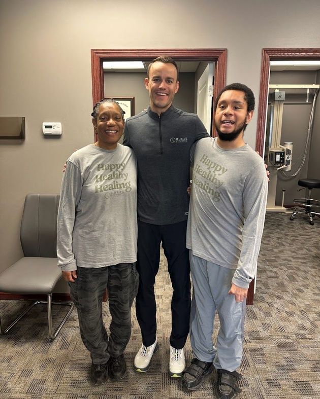 Three people posing indoors in front of mirrors, wearing matching gray long-sleeve shirts.