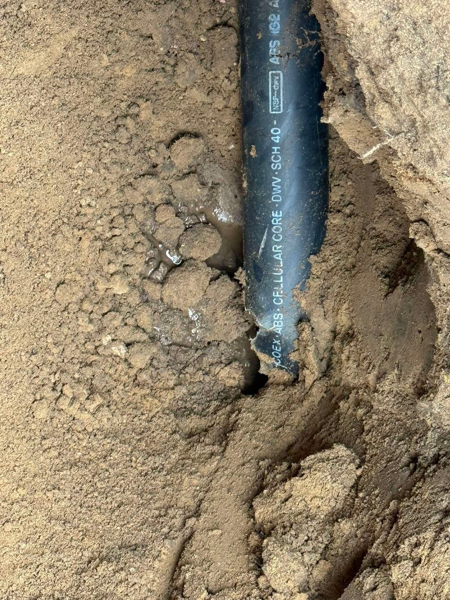 Black cable or pipe partially buried in tan dirt trench, with soil cracked around it