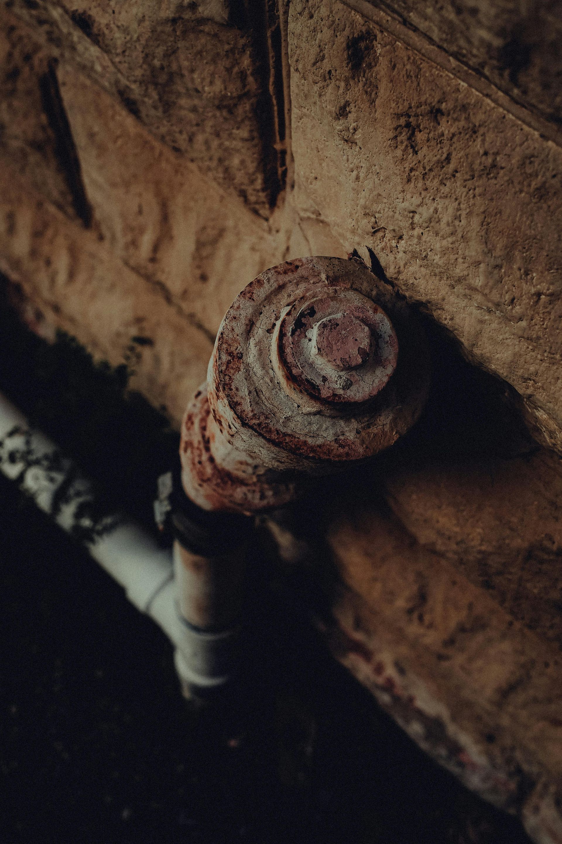 Rusty water valve on a stained wall, with a white pipe below.