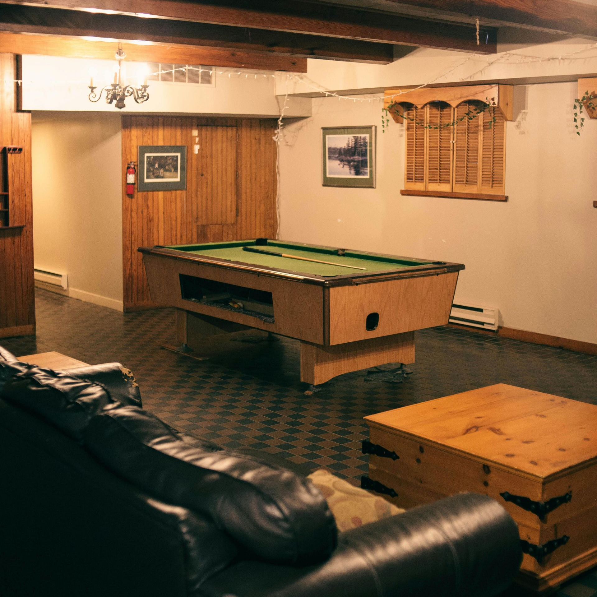A basement with a pool table, leather sofa, and wooden chest.