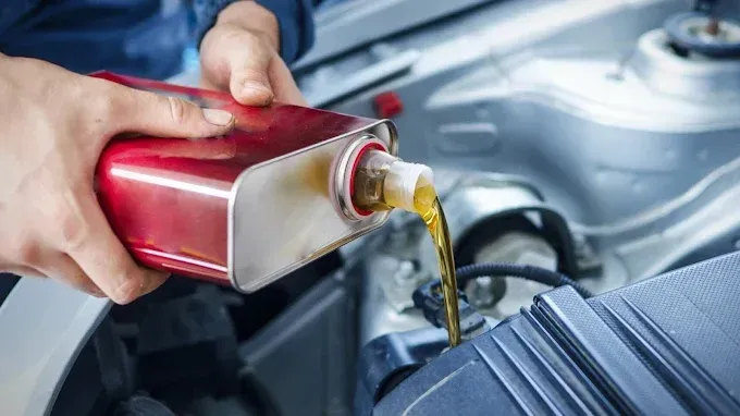 Verter manualmente aceite de motor de un recipiente rojo en el motor de un coche.