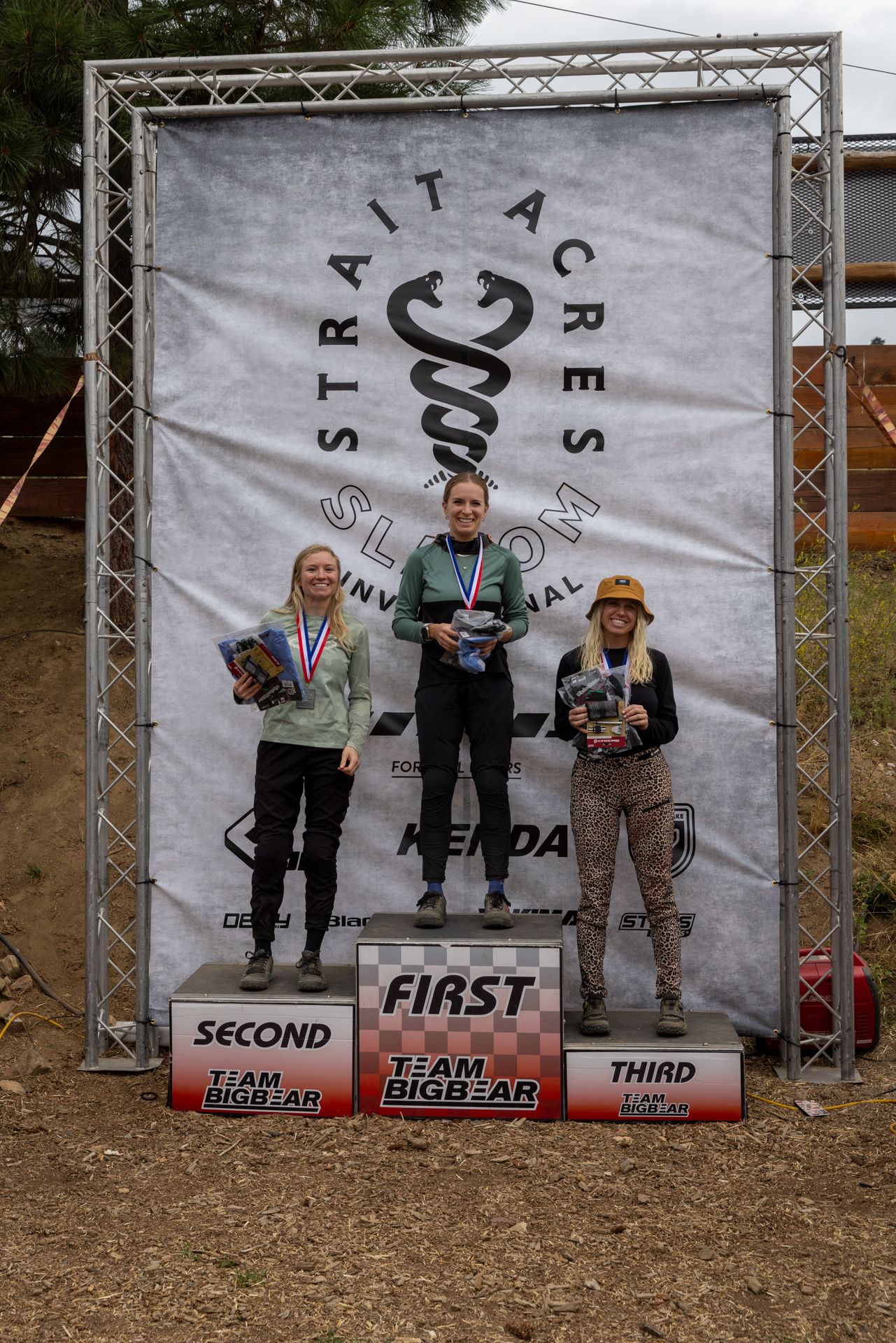 Podium with three women; winner in the middle holding a trophy. Event backdrop reads 