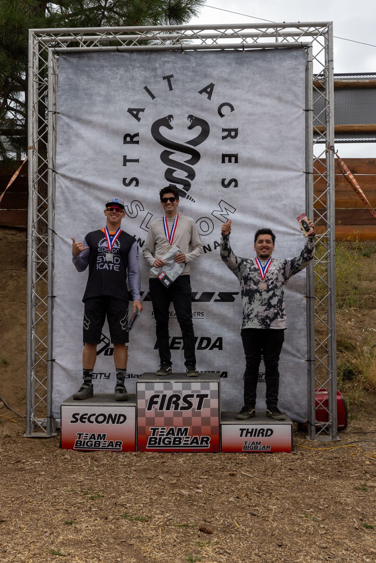 Podium with three men in athletic wear, holding trophies. 