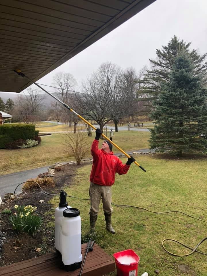 Person in red jacket spraying water from a long pole in a rainy yard next to a house