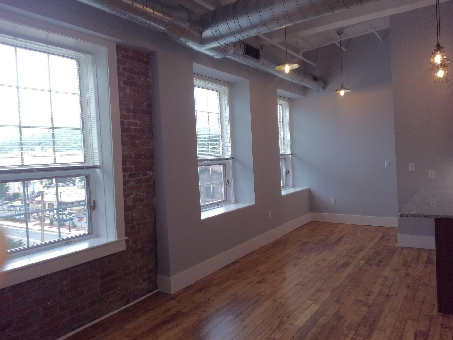 Empty loft-style room with brick wall, large windows, and hardwood floors