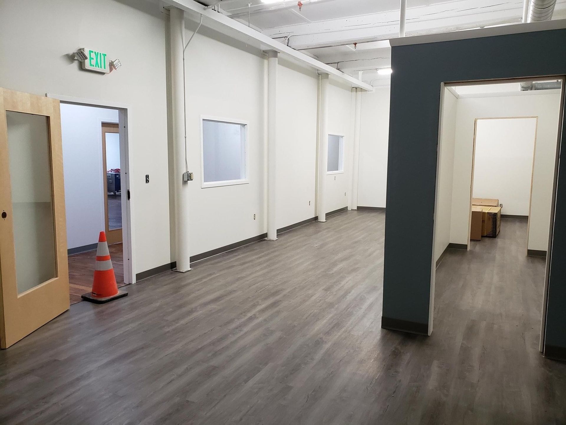 Empty office hallway with open doors, white walls, and gray wood flooring