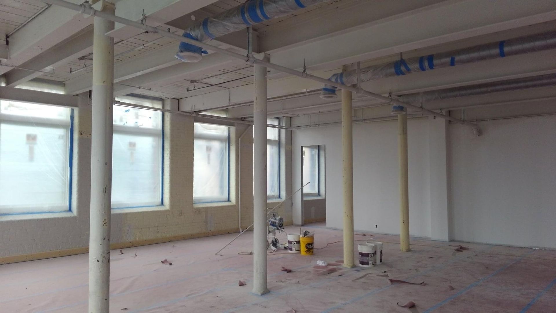 Empty unfinished office space with white columns, large windows, and construction tools on the floor