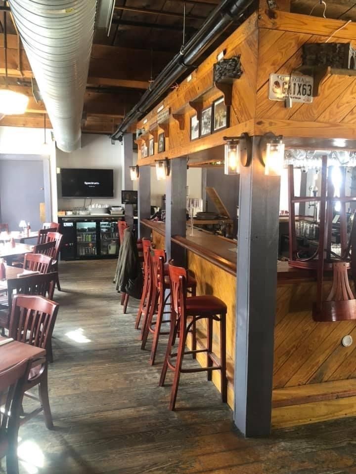 Empty restaurant interior with wooden bar stools, exposed ductwork, and a TV on the wall