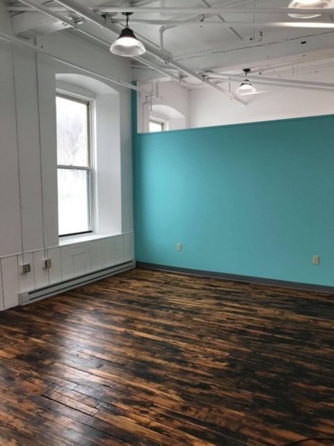 Empty room with teal accent wall, white walls, and wood-look floorboards in daylight.