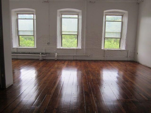 Empty room with polished hardwood floors and three arched windows letting in daylight.