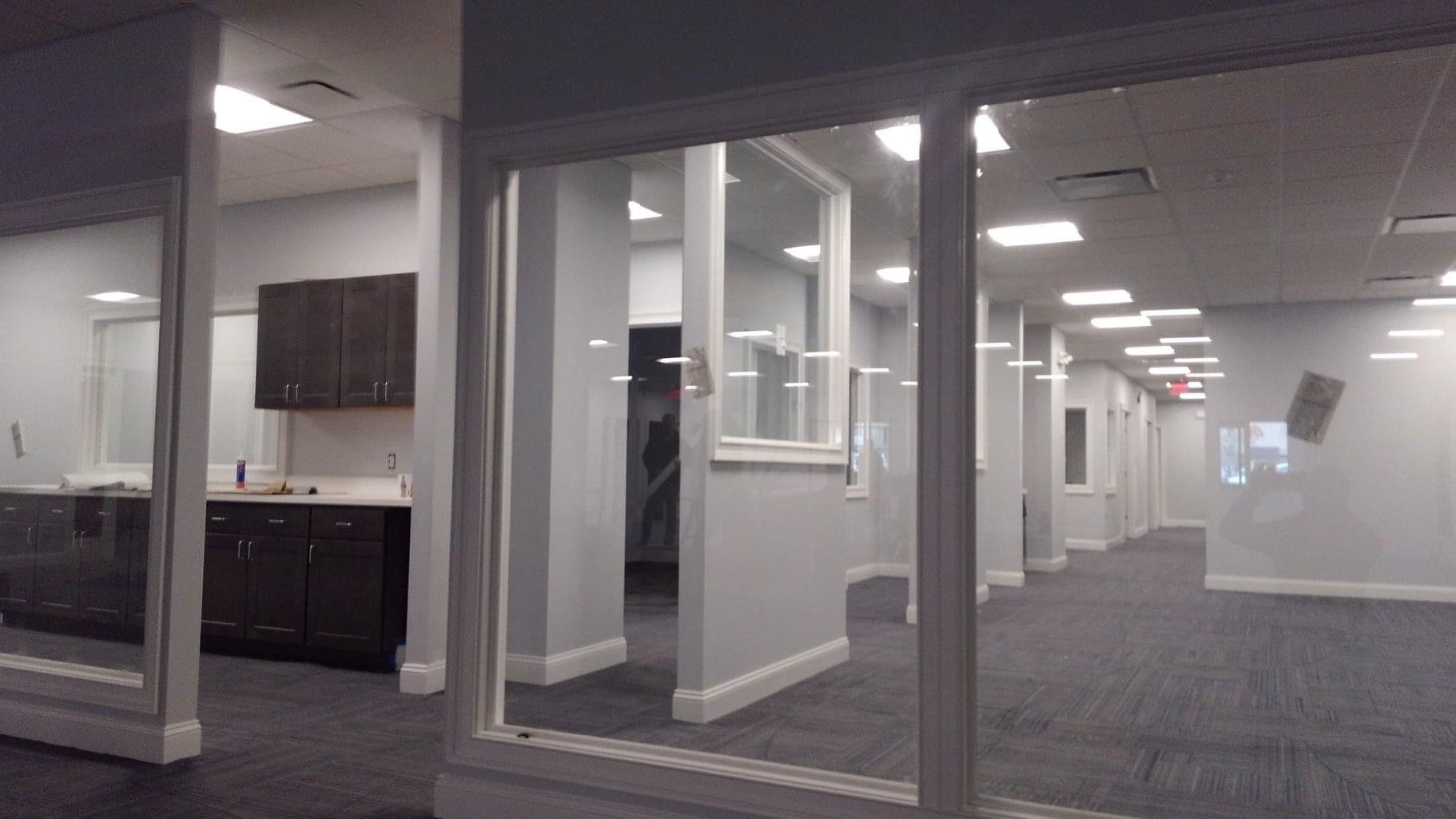 Empty office interior with glass partitions, gray carpet, and overhead fluorescent lights