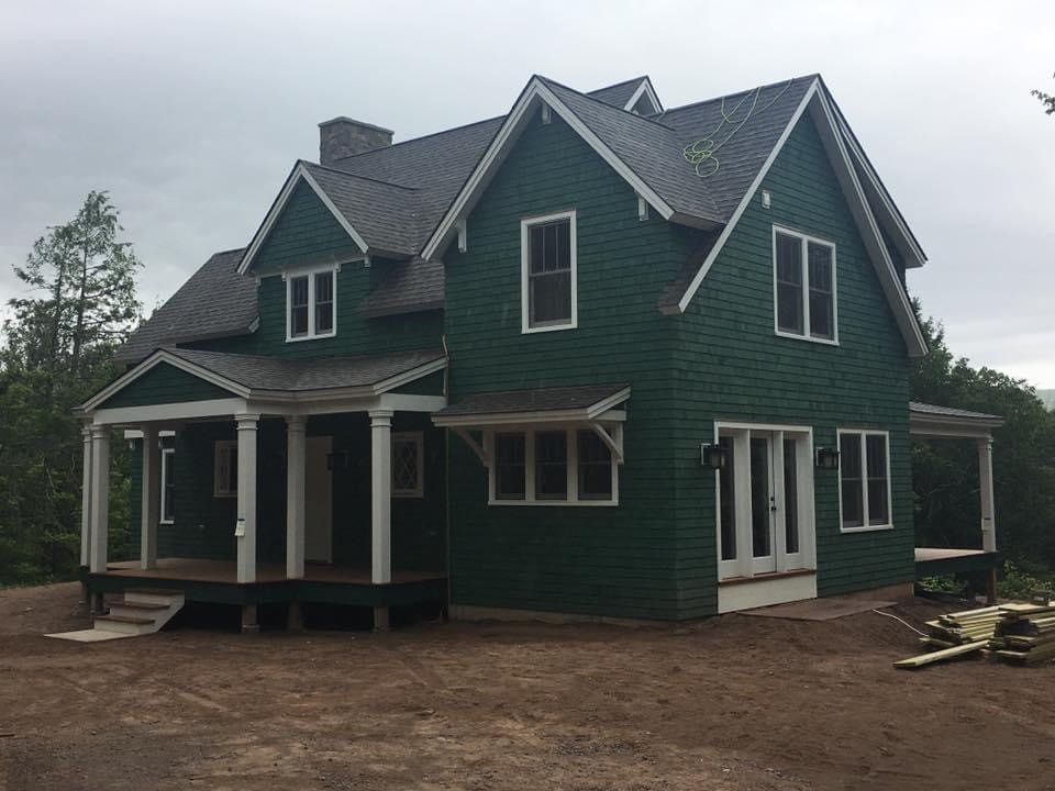 Green two-story house with white trim and porches under construction on a bare dirt lot