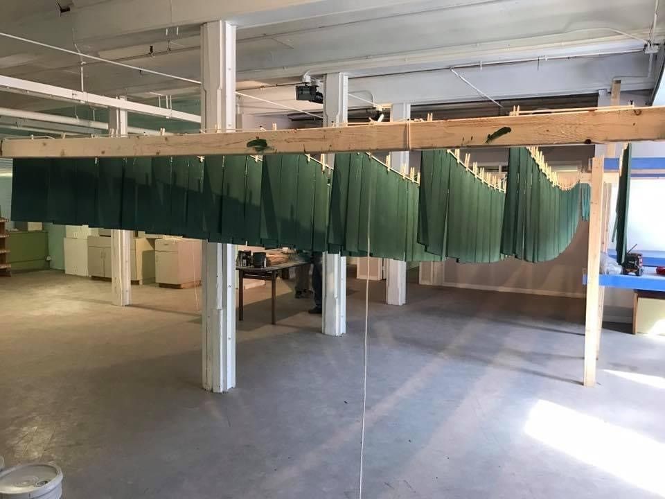 Long green hanging strips suspended in an industrial workshop with white columns and concrete floor