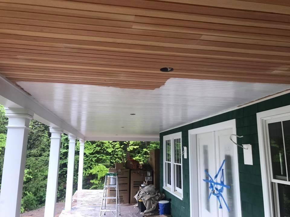 Covered porch with wood ceiling, white columns, green siding, and a ladder near the back wall.