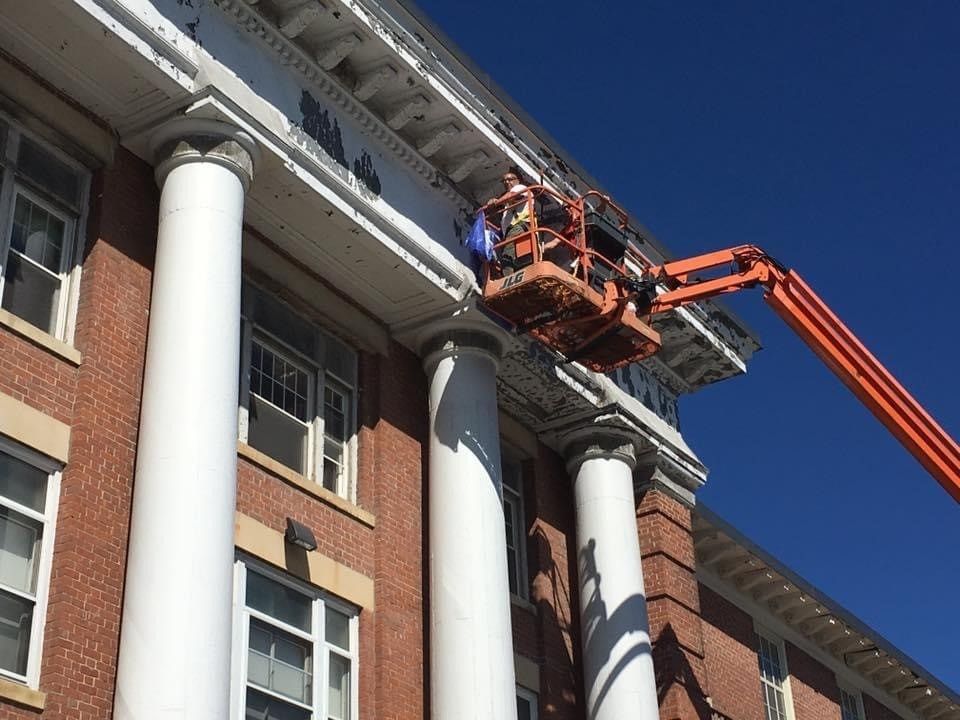 Worker on lift repairing a building facade with white columns and brick walls under a blue sky