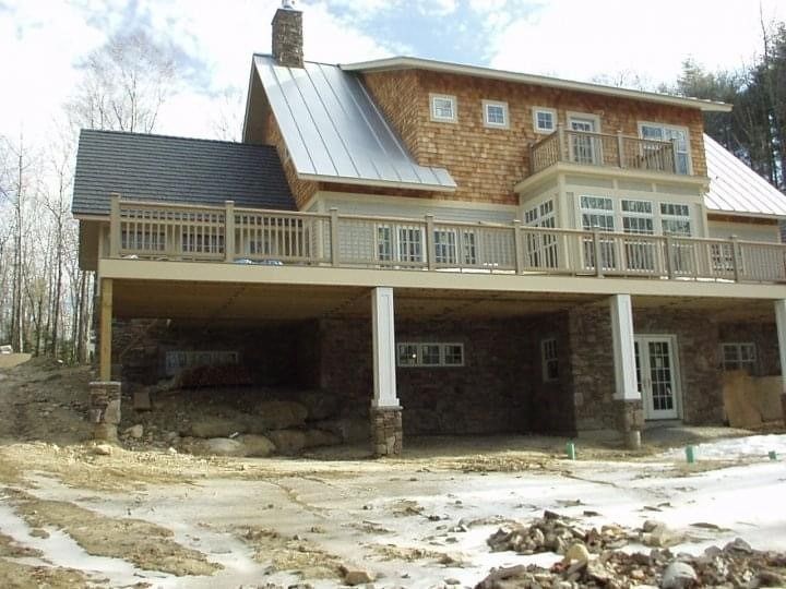 Large rustic house with stone and wood exterior, covered porch, and snow-covered ground